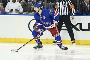 New York Rangers player skating with the puck while preparing to make a play during an NHL game.