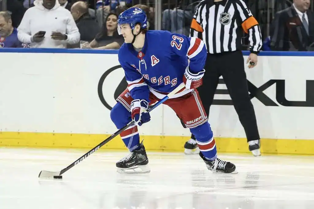 New York Rangers player skating with the puck while preparing to make a play during an NHL game.