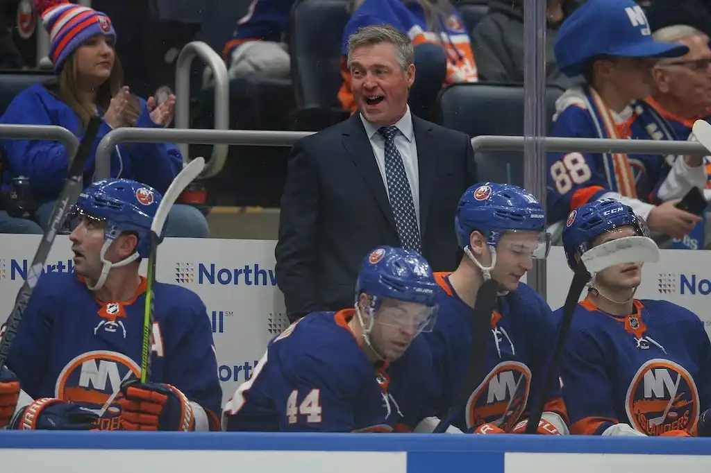 NHL 3 New York Islanders coach stands behind the bench, smiling.