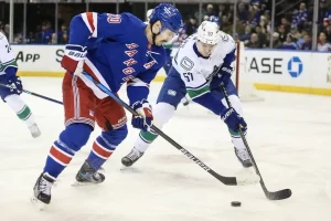 A New York Rangers player and an opposing player battle for the puck during a game.