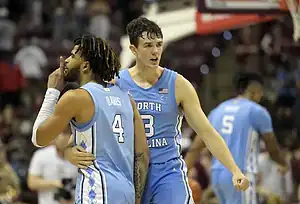 North Carolina basketball players celebrate on the court, with one player gesturing to the crowd while a teammate embraces him.