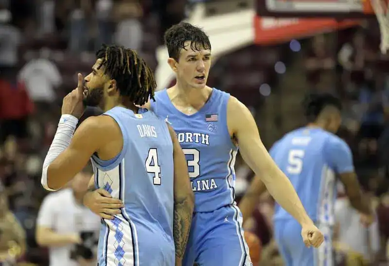 North Carolina basketball players celebrate on the court, with one player gesturing to the crowd while a teammate embraces him.