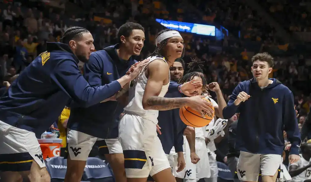 West Virginia Mountaineers players celebrate on the sideline during a game against the Oklahoma State Cowboys, showing excitement and energy on the court.