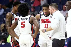Ole Miss Rebels basketball players gather in a huddle with their coach during a timeout.
