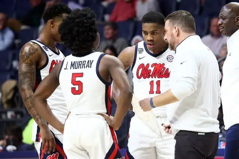 Ole Miss Rebels basketball players gather in a huddle with their coach during a timeout.