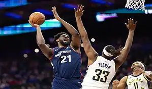 Philadelphia 76ers center driving to the basket against Indiana Pacers defender during an NBA game.