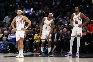 Three Phoenix Suns players stand on the court during a break in play.