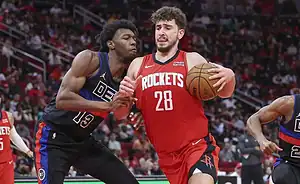 Houston Rockets player handling the ball while being closely defended by a Detroit Pistons player during an NBA game.