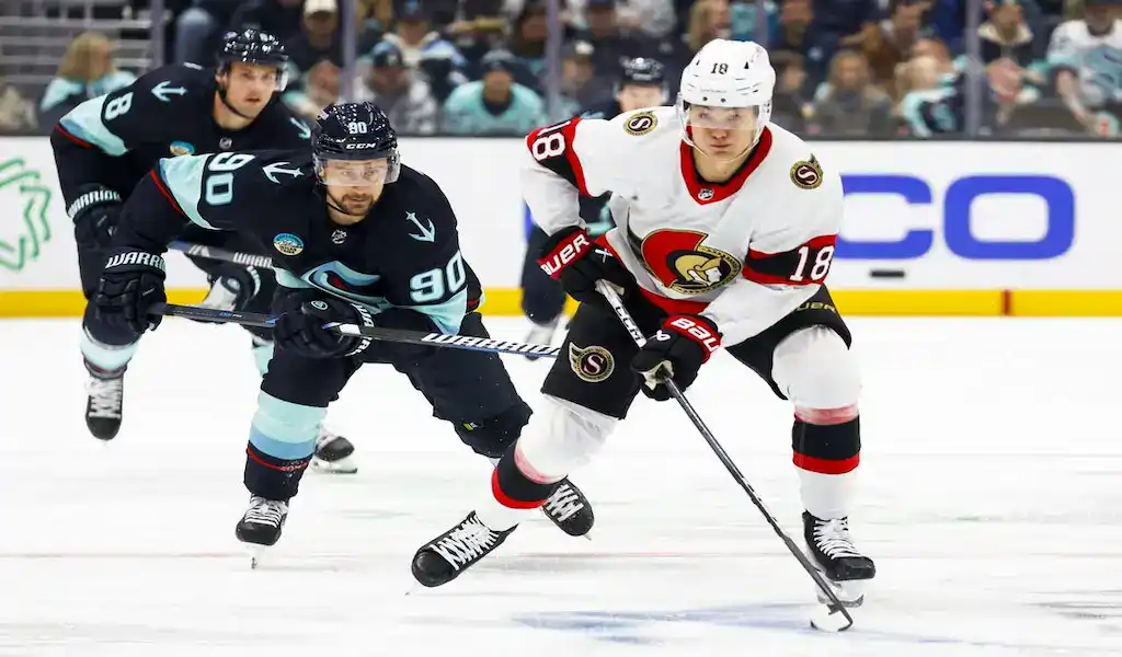 NHL 3 Ottawa Senators forward skates with the puck while pressured by Seattle Kraken defenders during an NHL game.