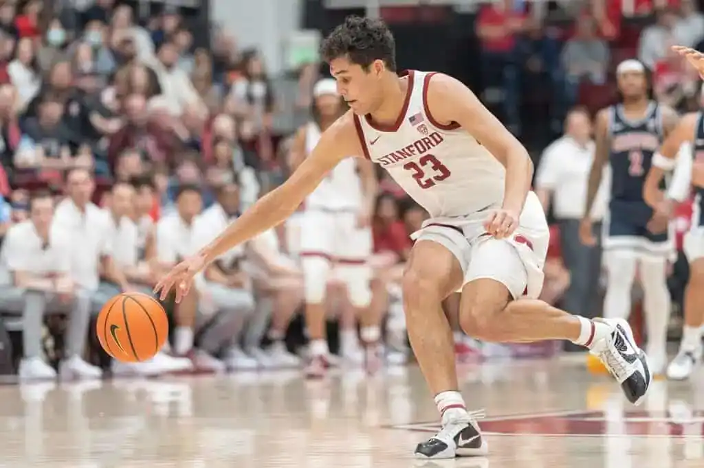 Stanford basketball player in a white jersey with number 23 dribbles the ball while moving quickly down the court during a game.