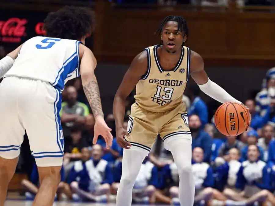 Georgia Tech player in gold uniform dribbles while facing a Duke defender.