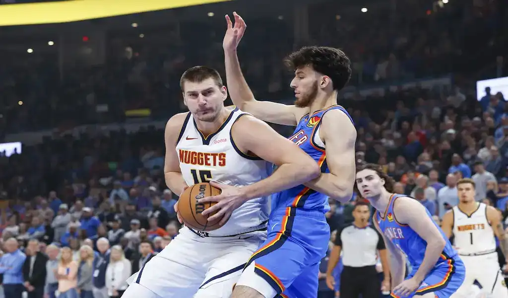 Denver Nuggets player drives to the basket while defended by an Oklahoma City Thunder player during an NBA game.