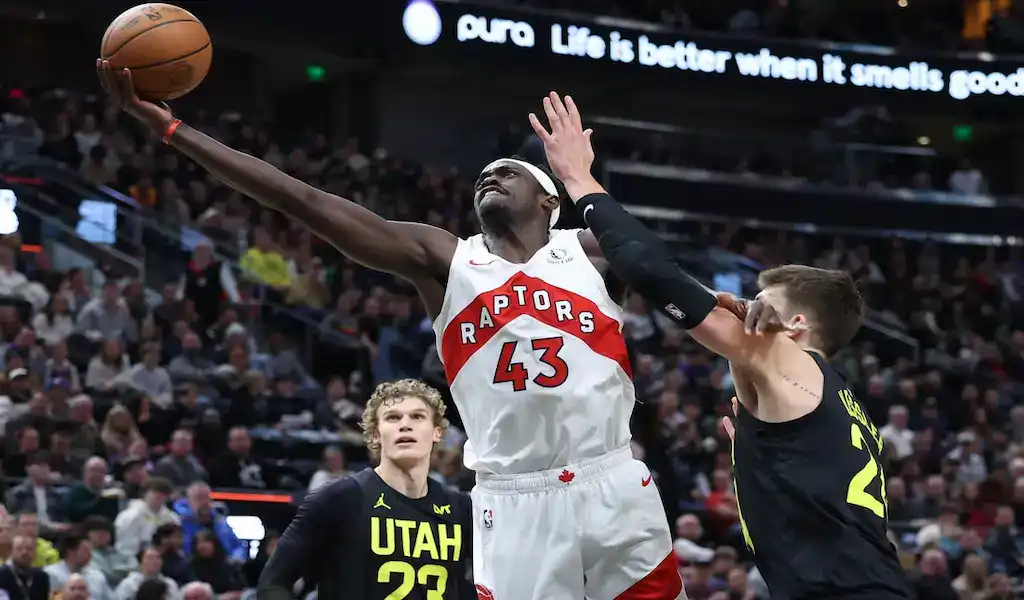 A Portland Trail Blazers player in a red and black uniform with number 0 driving to the basket, guarded by an Indiana Pacers player in a white and blue uniform with number 7, with a blurred crowd in the background, dated January 19, 2024.