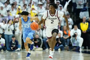 UConn player sprints down the court on a fast break while a defender chases closely behind.