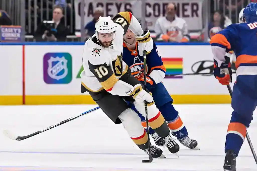 A Vegas Golden Knights player in white skates with the puck while defended by a New York Islanders player.