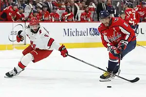 Washington Capitals forward skates with the puck while defended by a Carolina Hurricanes player.