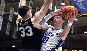 Duke Blue Devils player drives to the basket while defended by a Louisville Cardinals player during a college basketball game.