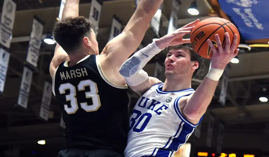 Duke Blue Devils player drives to the basket while defended by a Louisville Cardinals player during a college basketball game.