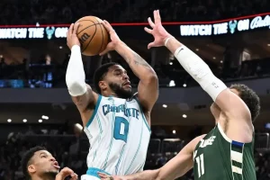 A Charlotte Hornets player rises for a jump shot over a Milwaukee Bucks defender.