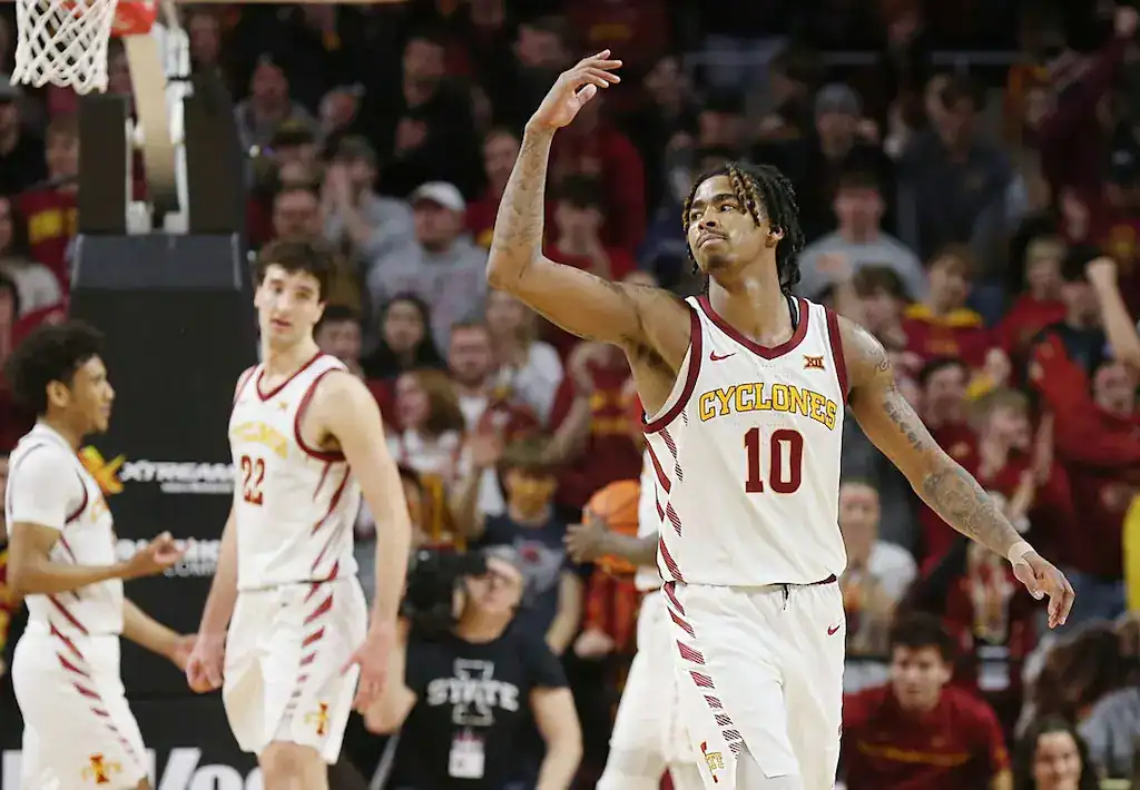 Iowa State Cyclones basketball player making a celebratory gesture on the court with teammates nearby.