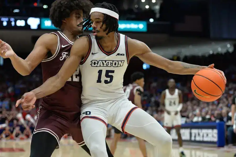 Dayton Flyers basketball player in a white uniform backs down a defender while holding the ball.