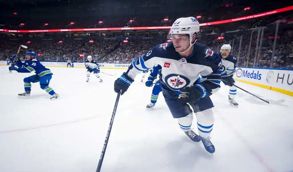 Winnipeg Jets player skates with the puck while pressured by Vancouver Canucks defenders during an NHL game.