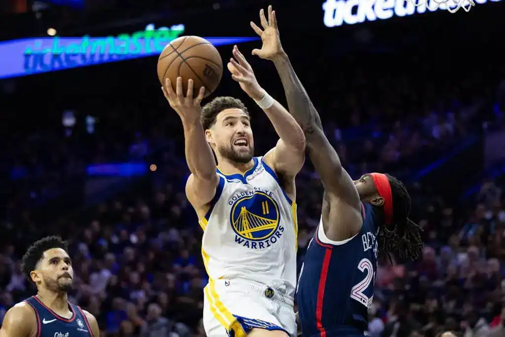 Golden State Warriors guard drives hard to the basket against a defender, extending for a layup attempt.