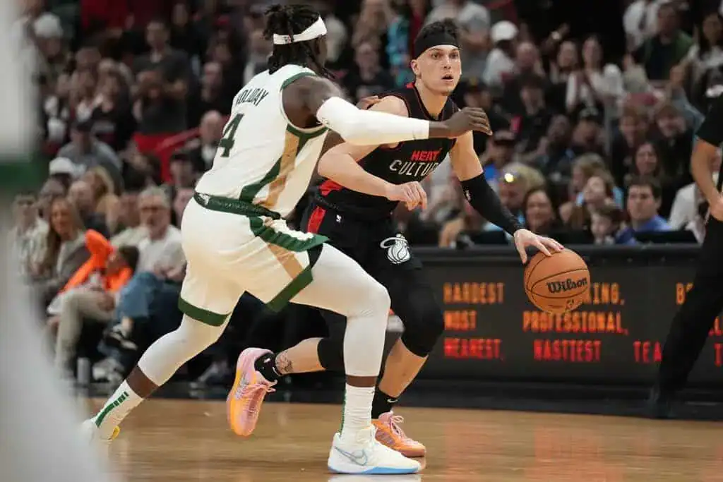 Miami Heat guard dribbling the basketball against Milwaukee Bucks defender Jrue Holiday during an NBA game.