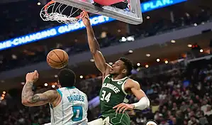 Milwaukee Bucks player dunking over Charlotte Hornets defender during an NBA game.