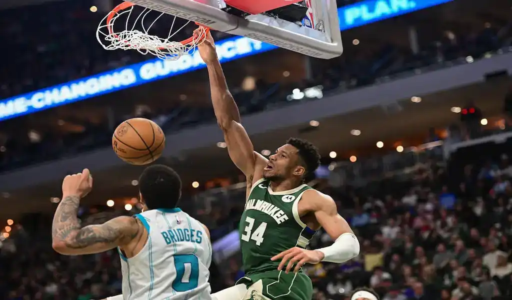 Milwaukee Bucks player dunking over Charlotte Hornets defender during an NBA game.