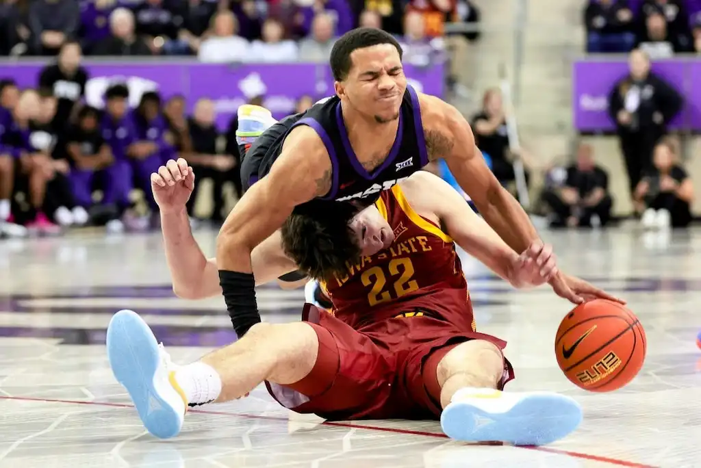 A Iowa State basketball player sits on the floor while an opposing player crashes into him during a scramble for the ball.