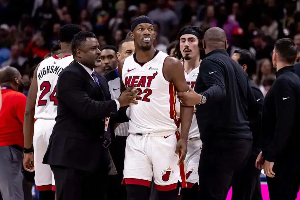 Miami Heat’s Jimmy Butler being held back by coaches and staff during a tense moment in a game.