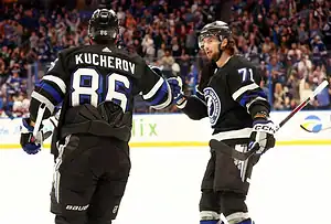 Tampa Bay Lightning players Nikita Kucherov and Anthony Cirelli celebrate on the ice in black uniforms.