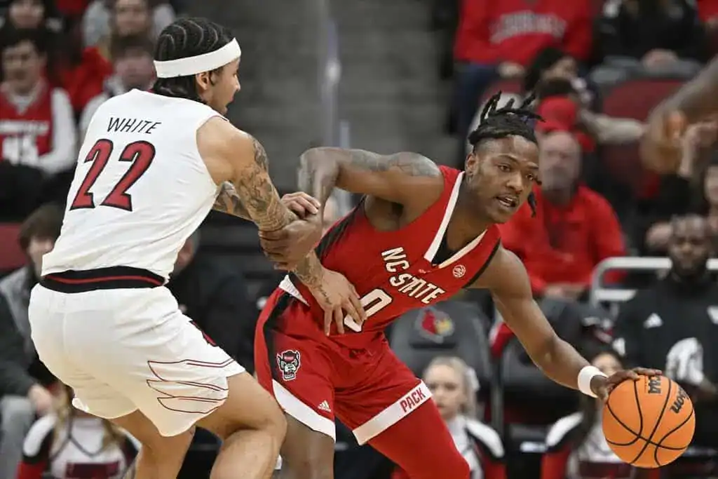 NC State player in red drives past a Boston College defender during a college basketball game.