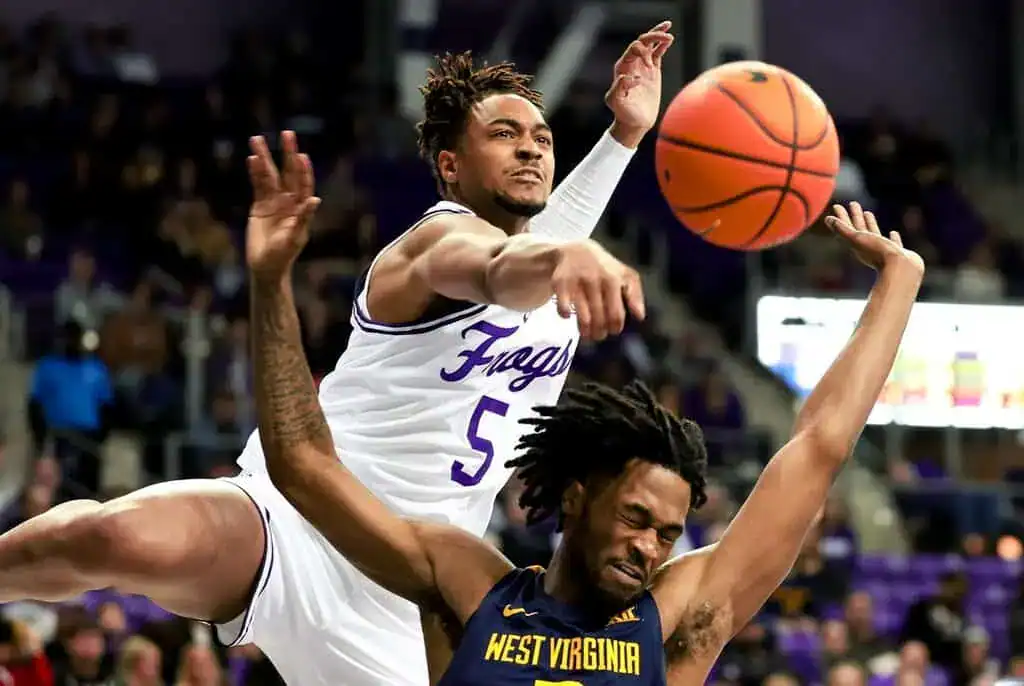 A basketball player in a white jersey leaps to block a shot, while another player in a navy jersey attempts to pass the ball.