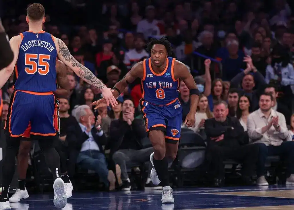 Two New York Knicks players celebrating a play with a high-five during an NBA game.