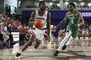 Florida Atlantic basketball player drives down the court while being chased by a North Texas defender.