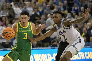 Oregon Ducks basketball player dribbles past UCLA Bruins defender during a game.