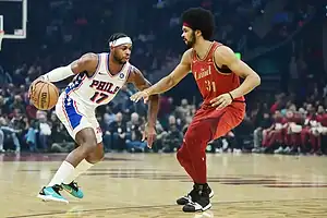 76ers player dribbles while being guarded by a Cavaliers player in a game.