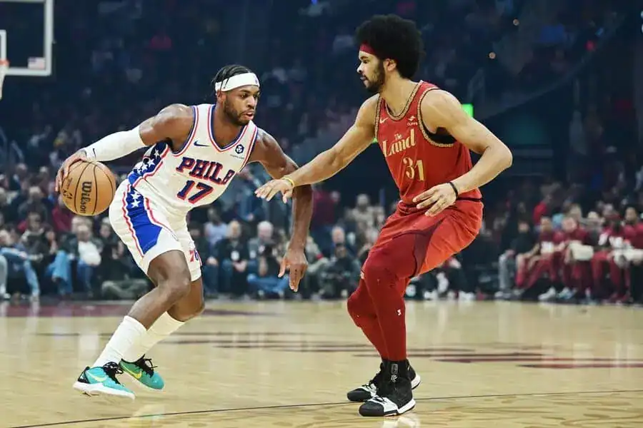 76ers player dribbles while being guarded by a Cavaliers player in a game.