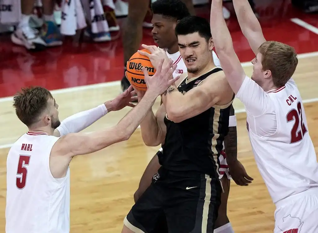 NCAAB 7 A Purdue player holds the ball tightly while being double-teamed by two defenders.
