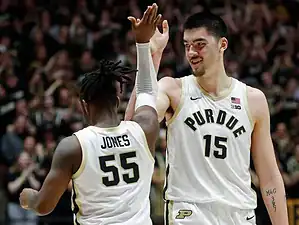 Purdue basketball players in white uniforms celebrate with a high five on the court.