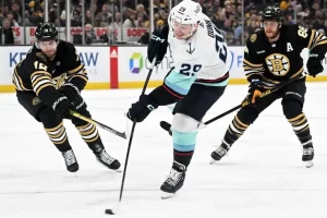 Seattle Kraken player takes a shot on goal while being defended by two Boston Bruins players.