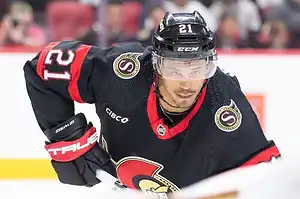 Ottawa Senators hockey player in a black jersey skates during a game, focused on the play.
