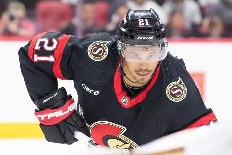 Ottawa Senators hockey player in a black jersey skates during a game, focused on the play.