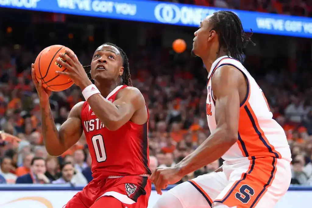NC State Wolfpack basketball player prepares to shoot against Syracuse Orange defender.