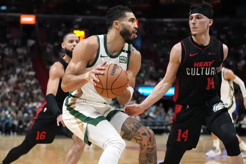 Boston Celtics forward Jayson Tatum holds the basketball, looking for a shot while being defended by a Miami Heat player.