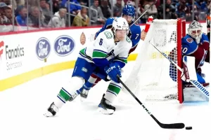 Vancouver Canucks player controls the puck behind the net while being closely pursued by a Colorado Avalanche defender.