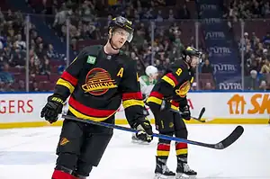 Vancouver Canucks players in black throwback jerseys skate on the ice during an NHL game.