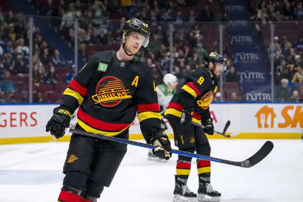 Vancouver Canucks players in black throwback jerseys skate on the ice during an NHL game.